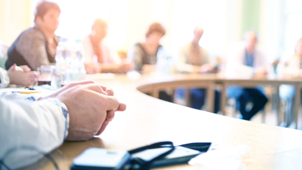 Blurred closeup of people sitting around curved boardroom table